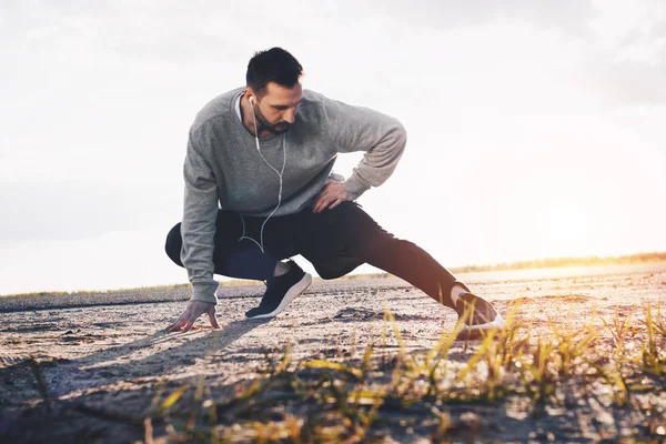 Athlete runner in headphones warmes up in the open air — Stock Photo, Image