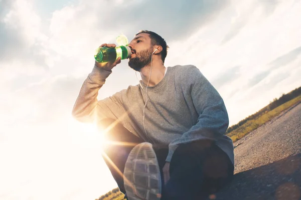 Idrottsman dricker vatten medan du sitter på asfalten och vila — Stockfoto