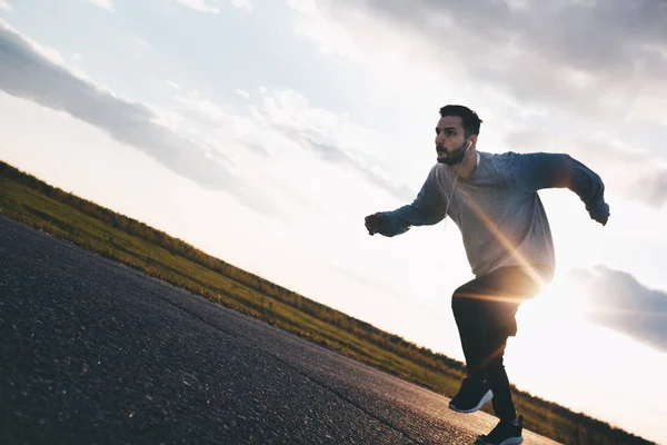 Man athlete in headphones quickly runs on a suburban road — Stock Photo, Image