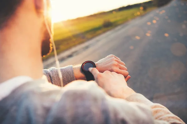 Joven atleta corredor en auriculares mira un reloj inteligente moderno — Foto de Stock