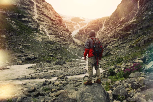 Young brave man with a backpack standing in front of a glacier