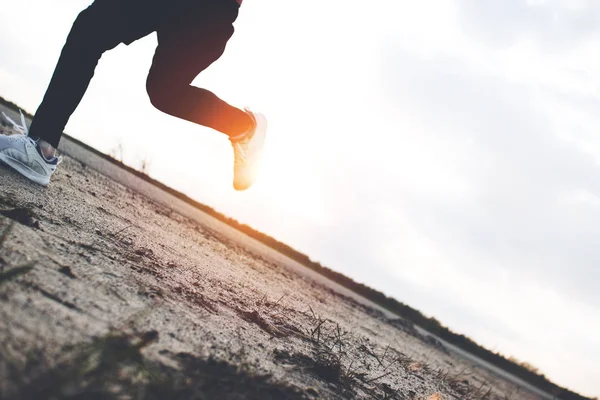 Patas de segundo y zapatillas de primer plano. Corriendo a través de la arena en el parque al atardecer — Foto de Stock