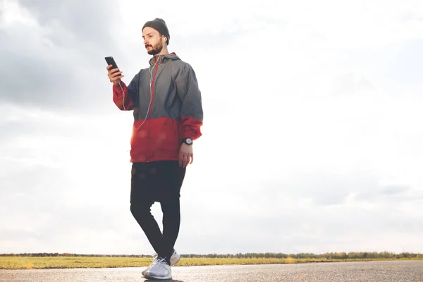 Спортсмен с умными часами и смартфоном в наушниках смотрит на гаджет — стоковое фото
