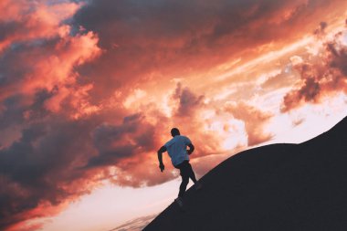 Atletik erkek üzerinde açık Sprint silüeti. Doğa günbatımı bir arka plan üzerinde çalışıyor. Kasıtlı koyu renkler