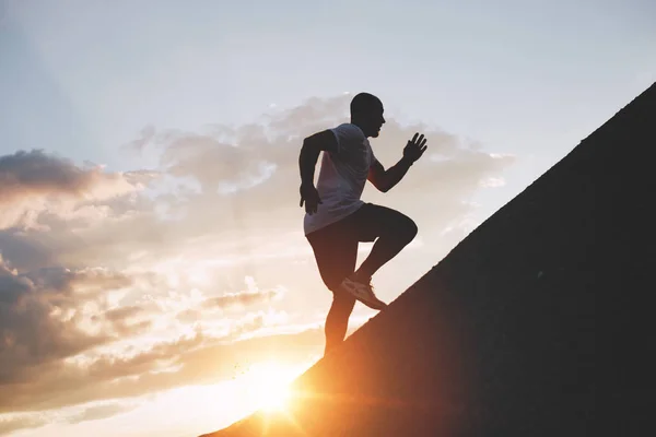 O corredor masculino treina em uma subida a uma montanha. Atleta corre pelas montanhas e colinas ao pôr do sol — Fotografia de Stock