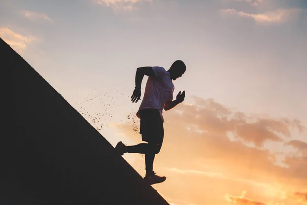 Un hombre fuerte corre por una colina empinada. El atleta se dedica a la aptitud física en la noche —  Fotos de Stock