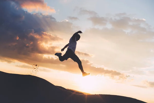 Silhouette eines Extremsportlers, der bei Sonnenuntergang Outdoor-Sport betreibt. Sportler springt über die Schlucht. Absichtlich dunkle Farben — Stockfoto