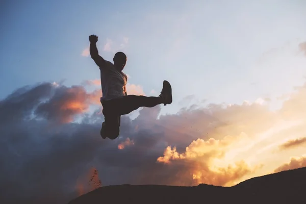 Silhouette eines Athleten, der vor dem Hintergrund schöner Wolken bei Sonnenuntergang springt. Sportler springt. Parkour, Freerun. Absichtlich dunkle Farben — Stockfoto