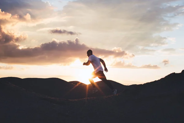 O atleta masculino treina ao ar livre. Correr ao pôr-do-sol ao ar livre. Silhueta de um corredor no fundo do belo pôr-do-sol — Fotografia de Stock