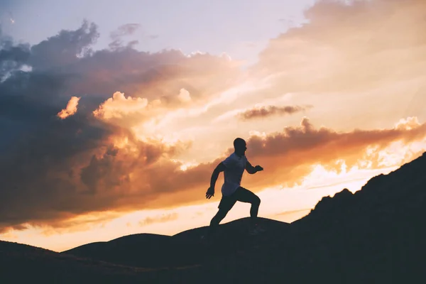 Silhouette eines starken Läufers vor dem Hintergrund des schönen Sonnenuntergangs im Freien. Fitnesstraining. Joggen in der Natur. Absichtlich dunkle Farben — Stockfoto