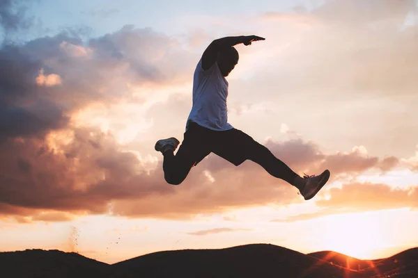 Strong and brave athlete jumps over a ditch. Silhouette of a man at the moment of a jump — Stock Photo, Image