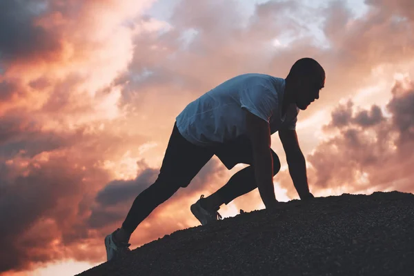 Man in start position ready for sprint. Outdoors workout. Fast running exercise. Sunset