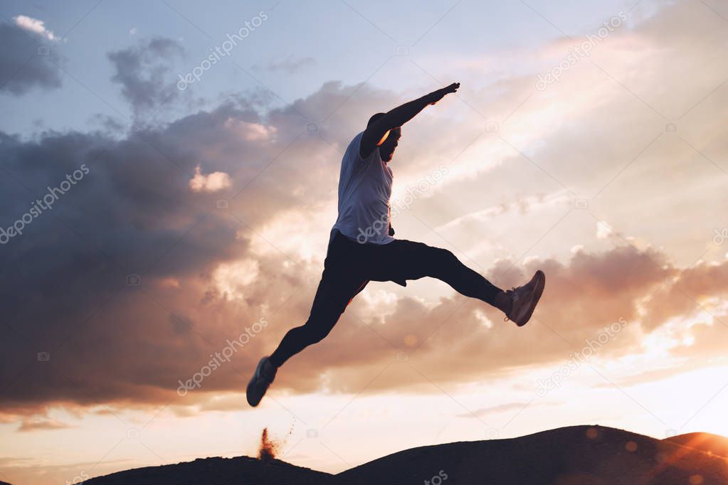 Sportsman is extreme in a jump on background of beautiful clouds at sunset. Parkour, freerun. Intentional dark colors