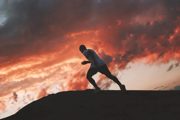 Сильний спортсмен тренується на свіжому повітрі ввечері на заході сонця. Чоловік-спортсмен біжить в гору. Намітний темний колір — стокове фото