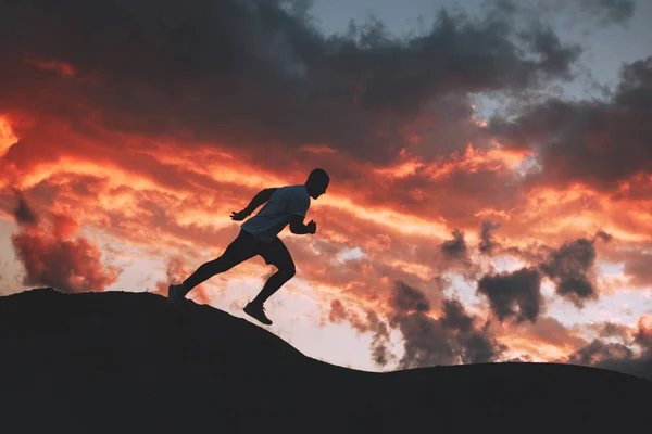 Silueta de un hombre dedicado a la aptitud en la naturaleza por la noche. Atleta corre rápidamente en las colinas de montaña desigual al atardecer — Foto de Stock