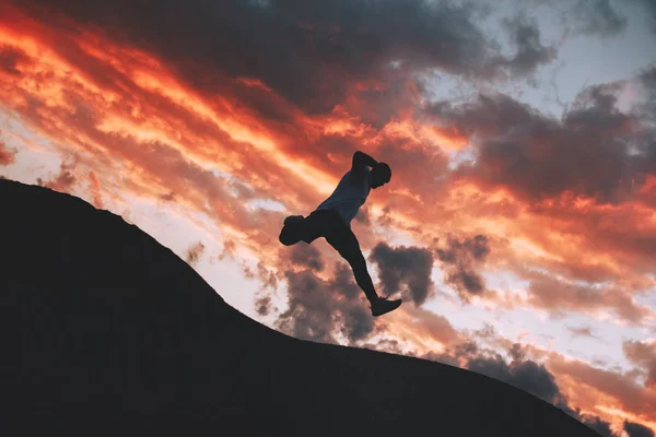 Człowiek działa i skoki nad górami i wzgórzami na tle o zachodzie słońca — Zdjęcie stockowe