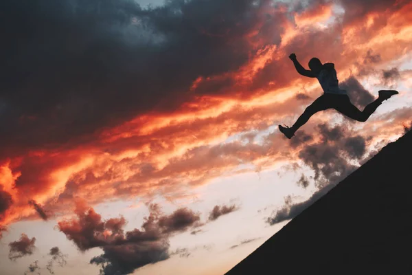 Silhouette of a brave male athlete jumping from the hill during a workout. Parkour and freerun — Stock Photo, Image