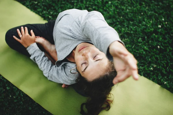 Žena cvičí jógu na zeleném trávníku. Mladá žena uvolňuje v józe pozice venku — Stock fotografie
