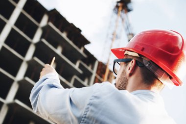 Genç işadamı gökdelen inşaatı yönlendirir. Mimar inşaat alanında inceler