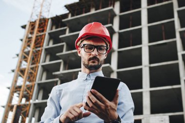 Tablet el ile genç iş adamı Oluşturucusu'nda kırmızı kask. Portre mühendis veya mimar ile şantiye tablete