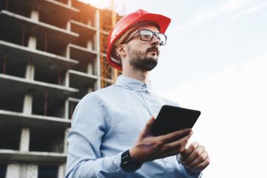 Modern mühendis veya mimar inşaat alanında elektronik tablet ile çalışır. Genç adam Oluşturucusu ile ev inşa bir arka plan üzerinde modern becerikli alet