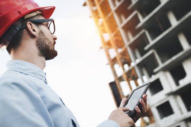 Genç işadamı Oluşturucu inşaat alanında modern elektronik tablet ile sakallı. Bitki endüstriyel yapı mimar görünüyor