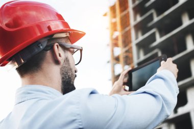 Şantiye mühendisi denetçisidir endüstriyel tesislerin inşası için. Elektronik tablet inşa edilen binanın arka planda tutan mimar portresi. oncept modern mühendis Oluşturucu ve sanayi
