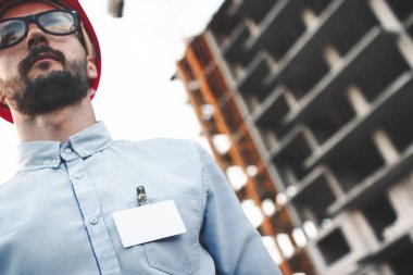 Modern inşaat mühendisi beyaz boş rozet veya kartvizit gömleğinin tesisi inşaatı arka plan üzerinde göğsünde ile portresi