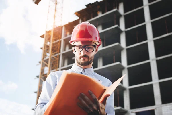 Ingeniero o arquitecto con una carpeta de documentos en mano. Inspector inspecciona el rascacielos en construcción — Foto de Stock