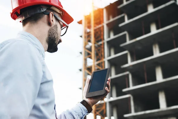 Ingeniero masculino profesional con tableta moderna en el sitio de construcción. Ingeniero moderno constructor comprueba en tableta electrónica programa de trabajo en la construcción de edificios modernos — Foto de Stock