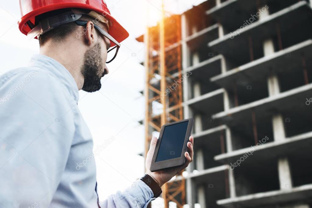Professional male engineer with modern tablet on construction site. Modern engineer builder checks on electronic tablet schedule of work on construction of modern building