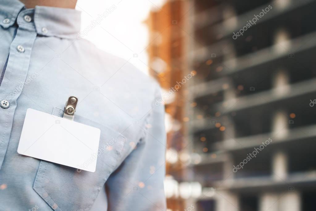 Blank white blank badge on businessman's shirt close-up on building construction background. Concept of white blank badge. Lens flare effect