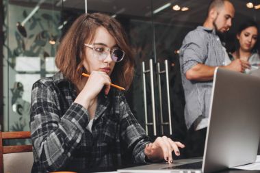 Dizüstü bilgisayarda çalışırken gözlük takan dalgın iş kadın fotoğrafı. Loft office ortak iş takım. Kalem tutan ve yeni başlangıç düşünme güzel kız