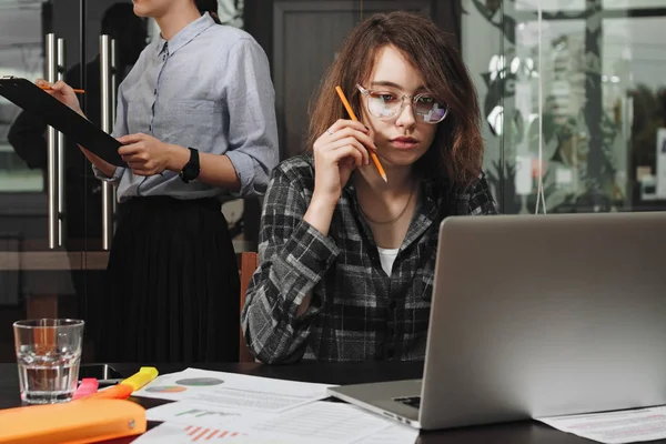 Tânăra femeie de afaceri în ochelari în proces de lucru pe laptop modern. Fotografia unei femei frumoase manager ocupat de lucru la un nou startup în loft office — Fotografie, imagine de stoc