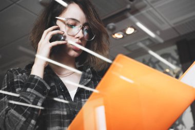 Bir şey Yöneticisi ile telefonda konuşurken gözlüklü genç dalgın iş kadını. Yakın çekim kadın smartphone cep telefonu ile modern ofis konuşma fotoğraf