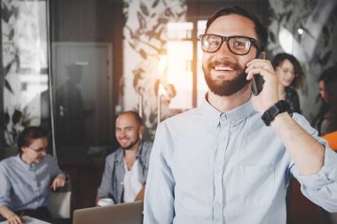 Fotoğraf yakın çekim genç gülümseyen iş takımı toplantı arka plan coworking smartphone konuşan bardaklarda işadamı sakallı. Yaratıcı yönetmen ile telefonda konuşan adam. Kasıtlı objektif mercek parlamaları