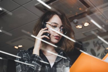 Office akşam ve Belgeler klasörüyle tutan geliştirme Direktörü ile telefonda konuşurken kadın yakın çekim fotoğrafı. Arka plan bulanık, küçük mercek parlaması