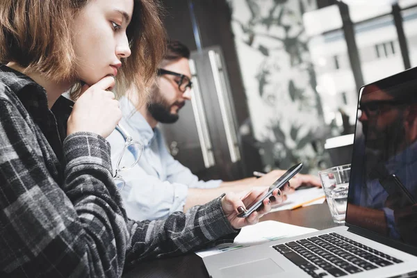 Joven empresaria con gafas y smartphone en la mano trabaja con laptop. Trabajar con dispositivos digitales en el espacio loft moderno — Foto de Stock