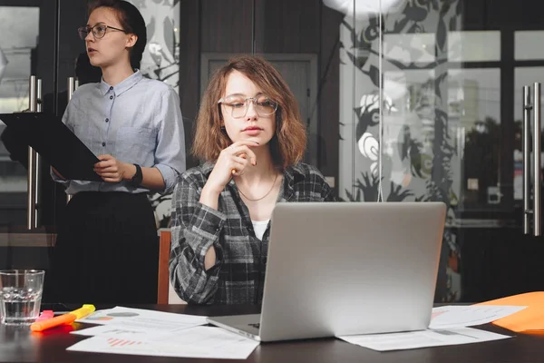 En ung forretningskvinne med briller som jobber med moderne laptop på loftskontoret. Foto av tenkende kvinnelig leder eller arkitekt som arbeider med nytt prosjekt – stockfoto