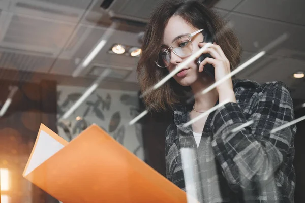 Yaratıcı dalgın Yöneticisi kadın uzmanı ile smartphone üzerinde konuşmak ve bir başlangıç tartışırken bardaklarda. Müşteri Hizmetleri veya destek iş kadını. Fotoğraf camı