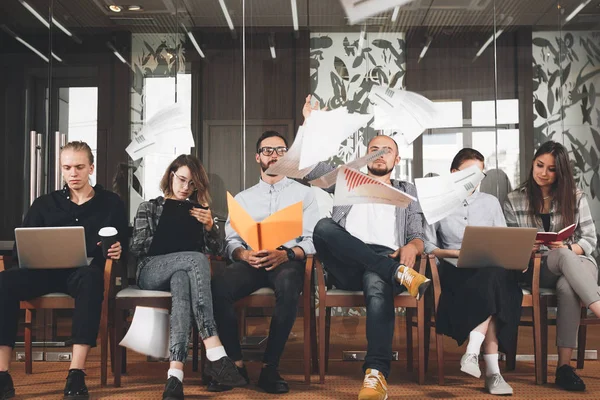 Grupo de gerentes creativos trabajan juntos en la oficina moderna. El hombre de negocios tira documentos de papel, el papel vuela por el espacio. Coworking people sit on chairs and conduct meeting — Foto de Stock