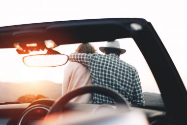 Erkek ve kadın cabriolet kaputa oturan ve gün batımı ve dağlar manzarayı