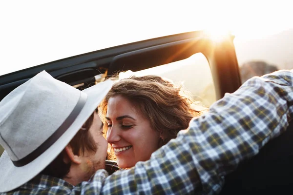 Boyfriend and girlfriend hugs in cabriolet car. Happy couple of hipsters having fun in convertible car on background of mountain landscape on sunset — Stock Photo, Image