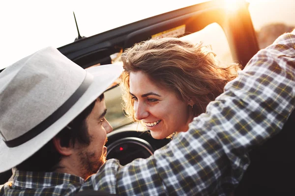 Young loving couple looking at each other sitting in car on background of mountain landscape and sunset. Happy loving couple in a cabriolet — Stock Photo, Image