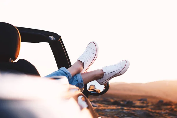 Young and successful traveler girl enjoy view and mountain landscape in sunlight from convertible car by hanging out her legs — Stock Photo, Image