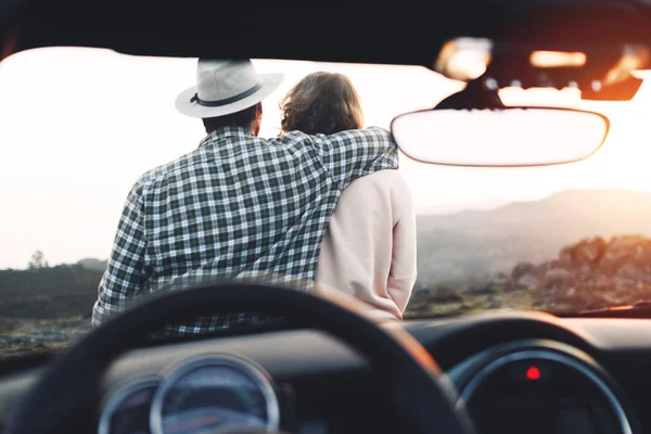 Ungt par i kærlighed nyde udsigten og slappe af sidder på hætten af cabriolet - Stock-foto