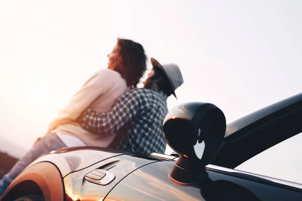 Moderna pareja amorosa de moda se sienta en la capucha de cabriolet y abrazos, parece puesta de sol — Foto de Stock