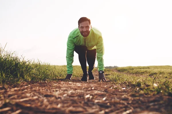 Un sportif en course pose sur le terrain. Athlète en tenue de sport et smartwatch est en préparation entraînement start run — Photo