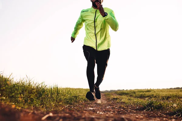 Strong male athlete running on trail in green field on outdoor. Sportsman fast run. Man jogging around on rough terrain on outdoor. Sport tight clothes