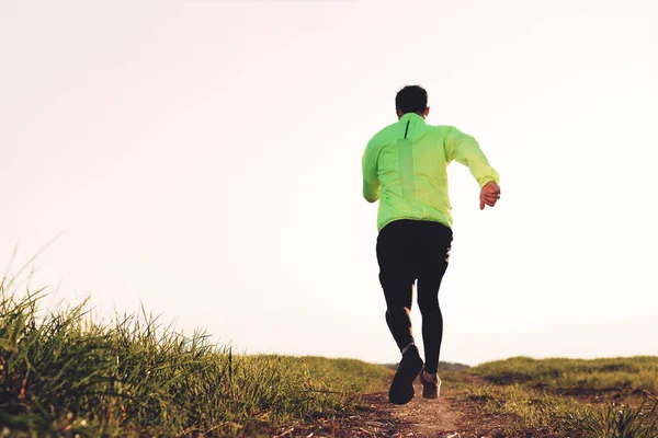 Спортсмен в современной спортивной одежде быстро бегает по тропе на зеленом поле — стоковое фото